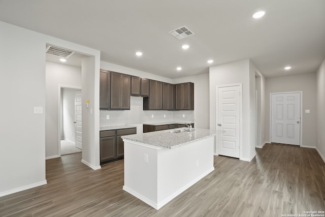 kitchen featuring decorative backsplash, an island with sink, light stone counters, hardwood / wood-style flooring, and sink