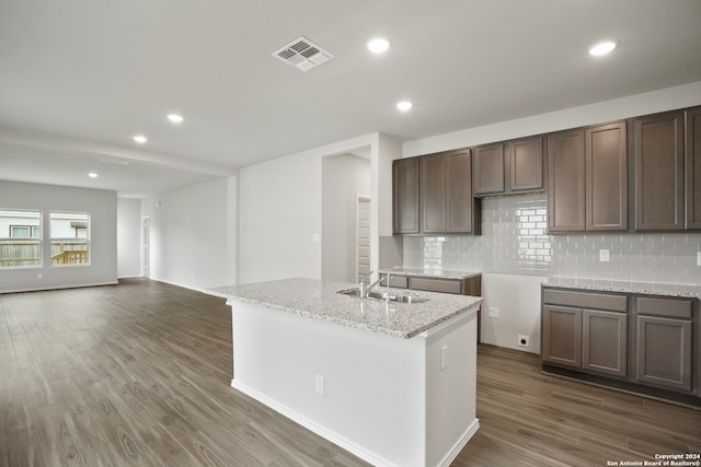 kitchen with dark hardwood / wood-style flooring, tasteful backsplash, an island with sink, light stone counters, and sink