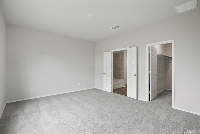 unfurnished bedroom with a spacious closet, a closet, carpet, and ensuite bathroom