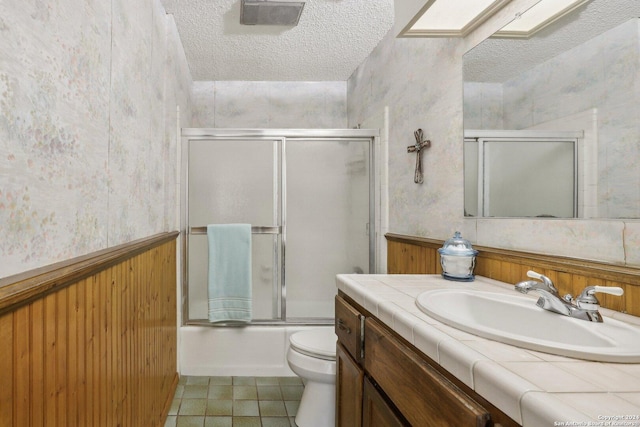 bathroom featuring shower / bath combination with glass door, toilet, wainscoting, a textured ceiling, and vanity