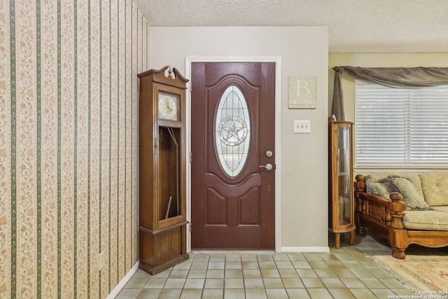 foyer entrance featuring light tile patterned flooring, a textured ceiling, and baseboards