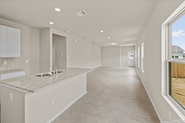 kitchen with backsplash, white cabinets, light stone counters, light tile patterned floors, and sink