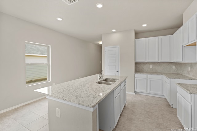 kitchen featuring decorative backsplash, white cabinetry, sink, an island with sink, and light tile patterned floors