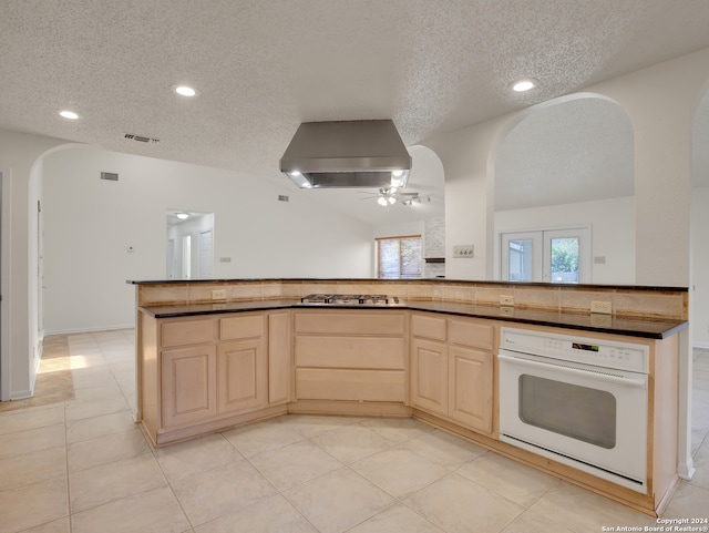 kitchen with wall chimney range hood, white oven, ceiling fan, and light tile patterned floors