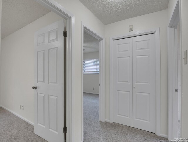 corridor with a textured ceiling and light colored carpet