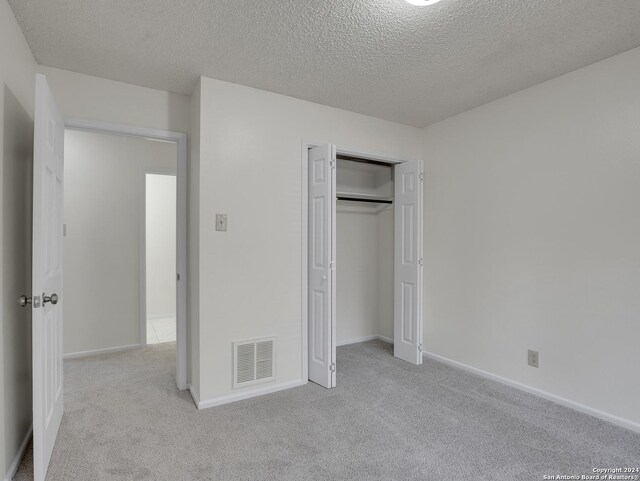 unfurnished bedroom with a textured ceiling, a closet, and light carpet