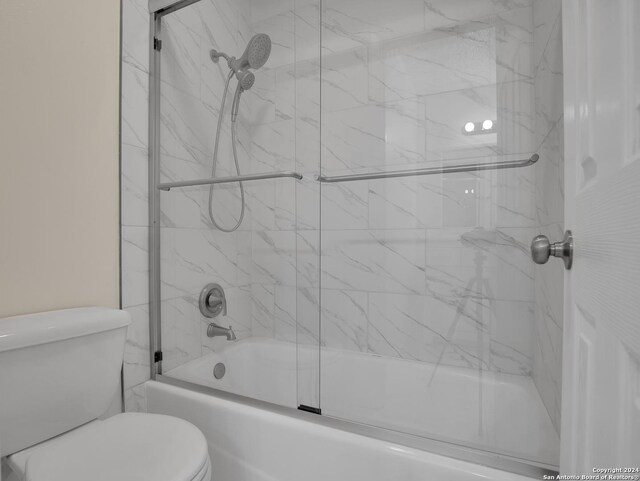 bathroom featuring toilet and combined bath / shower with glass door