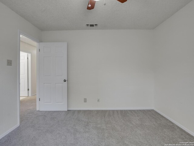 spare room featuring ceiling fan, light colored carpet, and a textured ceiling