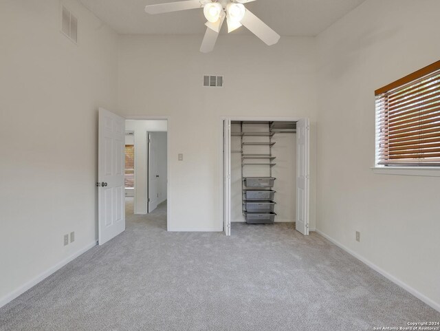 unfurnished bedroom featuring light colored carpet, a closet, a high ceiling, and ceiling fan