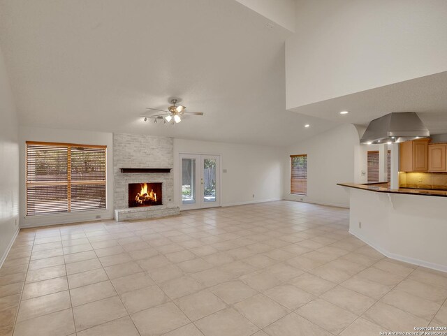 unfurnished living room featuring light tile patterned floors, a fireplace, vaulted ceiling, ceiling fan, and brick wall