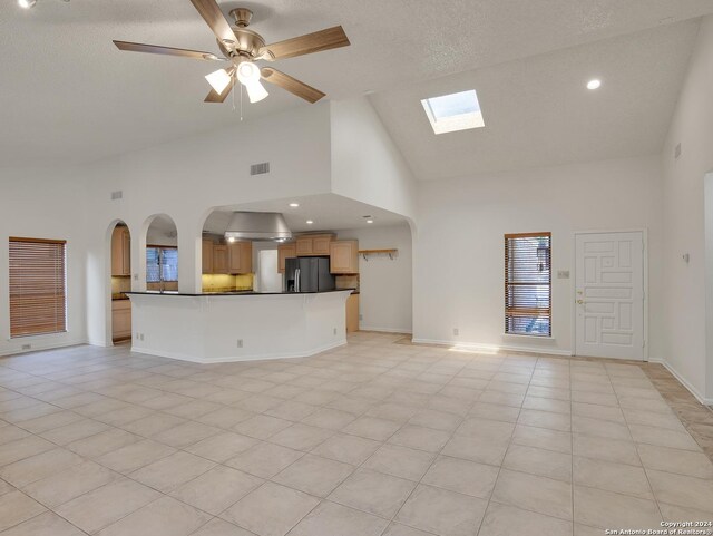 unfurnished living room featuring ceiling fan, high vaulted ceiling, a skylight, and light tile patterned floors