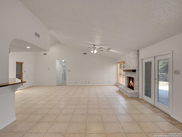 unfurnished living room featuring light tile patterned floors, high vaulted ceiling, a fireplace, a textured ceiling, and ceiling fan