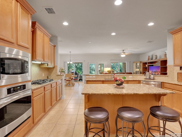 kitchen featuring decorative backsplash, a kitchen breakfast bar, light brown cabinetry, appliances with stainless steel finishes, and kitchen peninsula