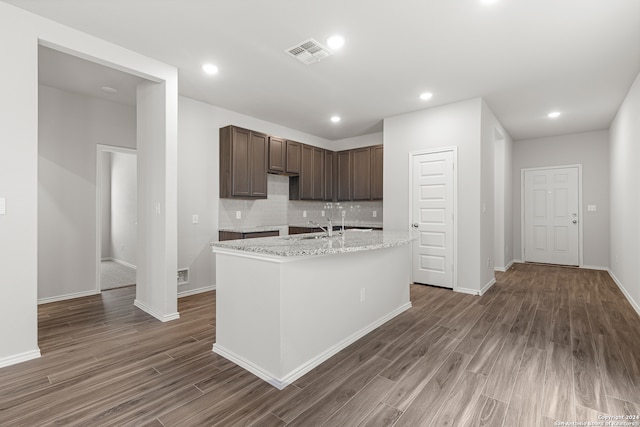 kitchen featuring decorative backsplash, sink, an island with sink, light stone countertops, and dark hardwood / wood-style flooring