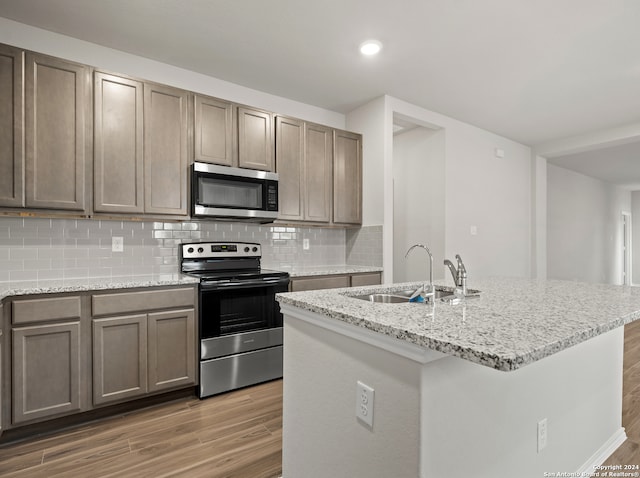 kitchen featuring hardwood / wood-style floors, appliances with stainless steel finishes, backsplash, and light stone countertops