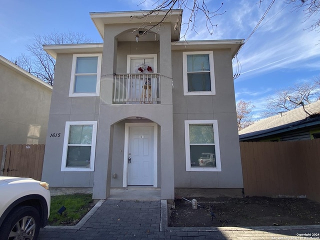 view of front of home featuring a balcony, fence, and stucco siding