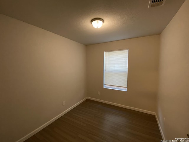 unfurnished room featuring visible vents, baseboards, a textured ceiling, and dark wood finished floors