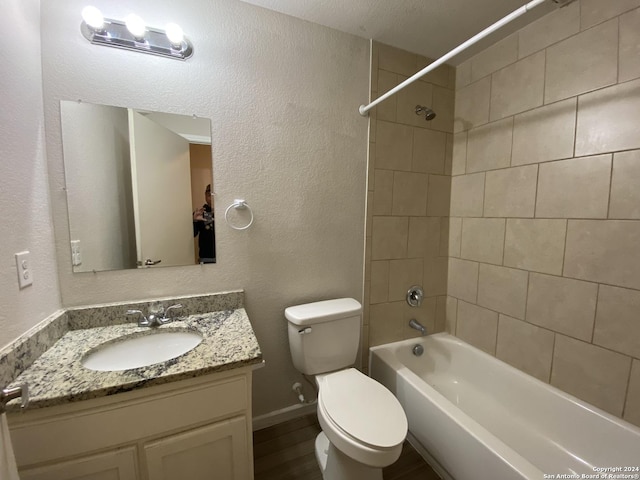 bathroom featuring toilet, shower / tub combination, wood finished floors, vanity, and a textured wall