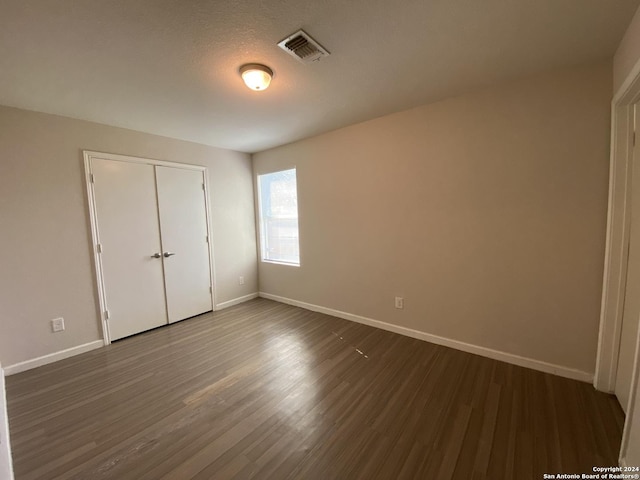 unfurnished bedroom with baseboards, visible vents, dark wood-type flooring, a closet, and a textured ceiling