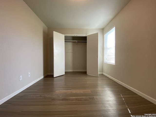 unfurnished bedroom featuring dark wood-style floors, a closet, and baseboards