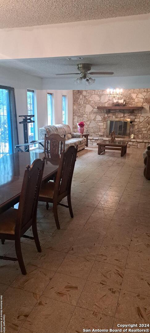 dining area featuring a textured ceiling, a stone fireplace, and ceiling fan