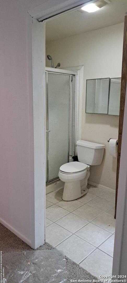 bathroom with tile patterned floors, a shower with shower door, and toilet