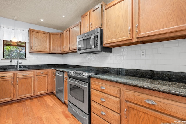 kitchen with appliances with stainless steel finishes, light hardwood / wood-style floors, decorative backsplash, sink, and dark stone counters