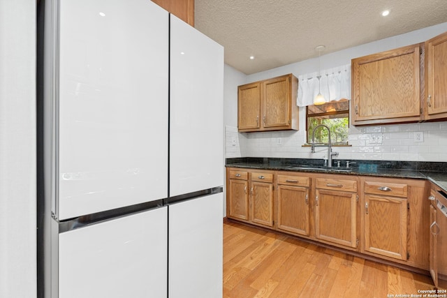 kitchen featuring light wood-type flooring, decorative backsplash, white refrigerator, sink, and a textured ceiling