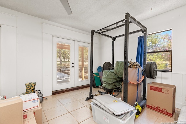 workout area featuring a textured ceiling, light tile patterned flooring, and a healthy amount of sunlight