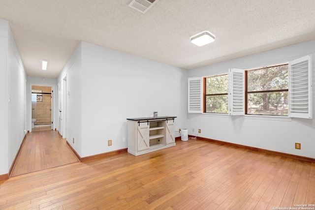 unfurnished room with a textured ceiling and light wood-type flooring