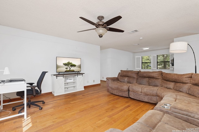 living room featuring ceiling fan, light wood-type flooring, and a textured ceiling