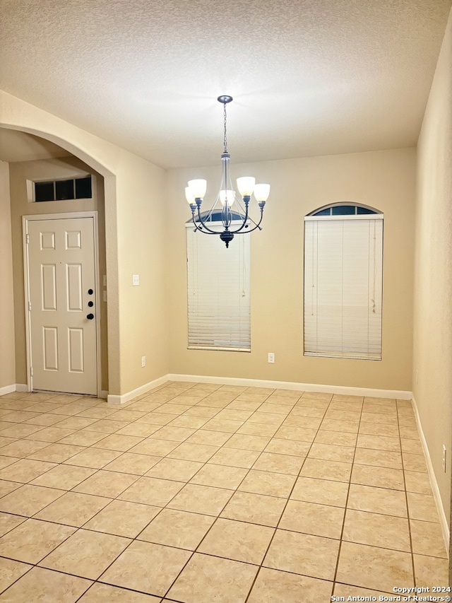 unfurnished dining area with a textured ceiling, a notable chandelier, and light tile patterned floors