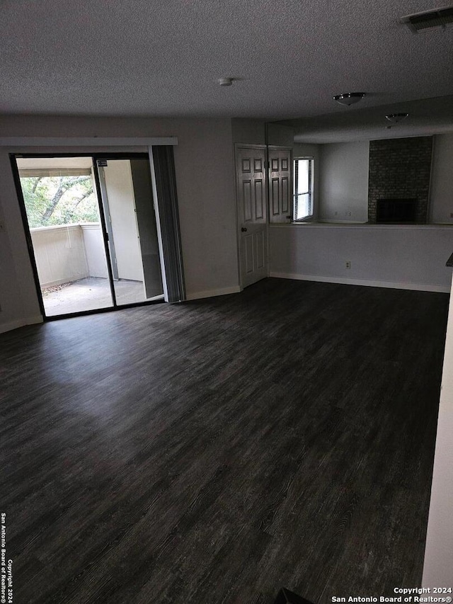 empty room with a textured ceiling, a large fireplace, and dark hardwood / wood-style floors