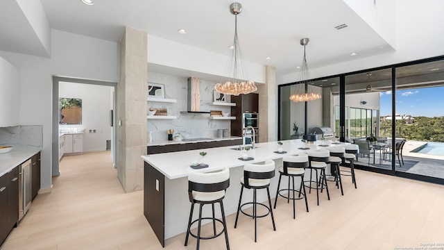 kitchen with a kitchen island with sink, backsplash, hanging light fixtures, and light hardwood / wood-style flooring