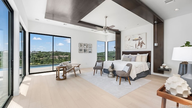 bedroom featuring ceiling fan, a raised ceiling, light hardwood / wood-style flooring, and access to outside