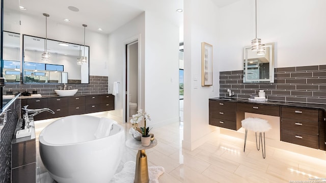 bathroom with backsplash, a tub to relax in, tile patterned floors, vanity, and tile walls