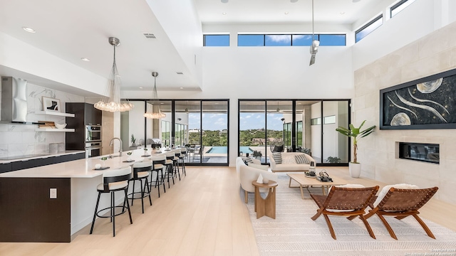 living room featuring light hardwood / wood-style flooring, a high ceiling, a tiled fireplace, sink, and a notable chandelier