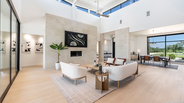 living room featuring a high ceiling, a fireplace, light hardwood / wood-style floors, tile walls, and ceiling fan