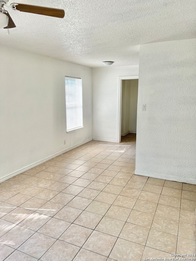 empty room with ceiling fan, light tile patterned floors, and a textured ceiling