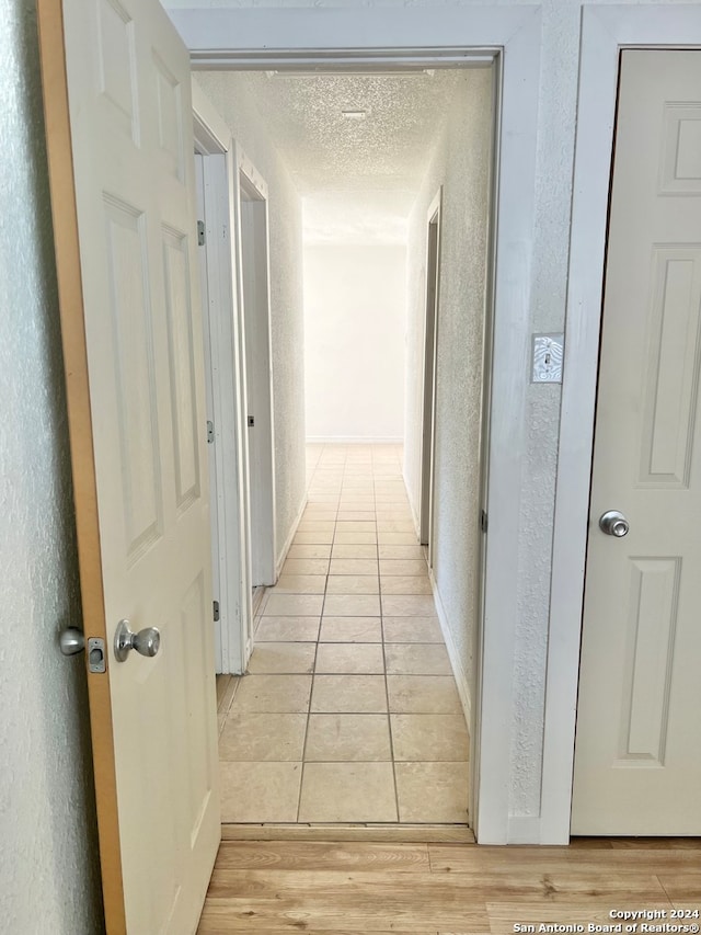 hallway with a textured ceiling and light tile patterned flooring