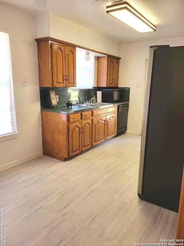 kitchen featuring sink, tasteful backsplash, light hardwood / wood-style flooring, and black appliances