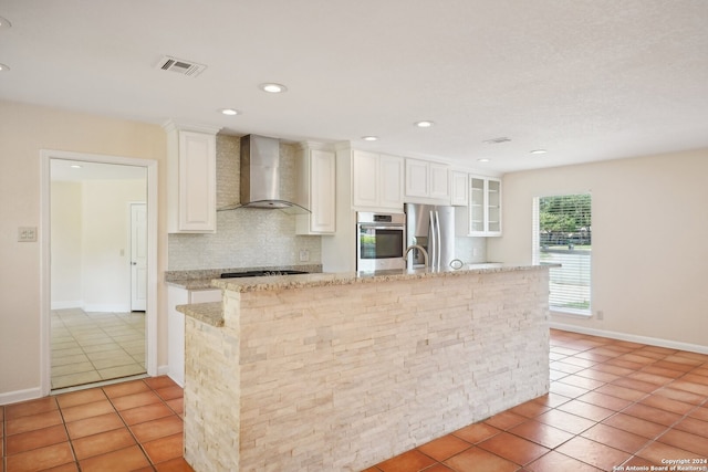 kitchen with backsplash, stainless steel appliances, light stone counters, wall chimney range hood, and light tile patterned floors