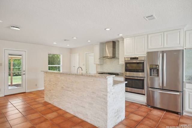 kitchen with wall chimney exhaust hood, decorative backsplash, a textured ceiling, light tile patterned floors, and stainless steel appliances