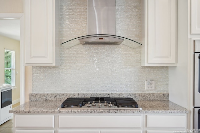 kitchen featuring stainless steel gas cooktop, white cabinets, wall chimney exhaust hood, and light stone countertops