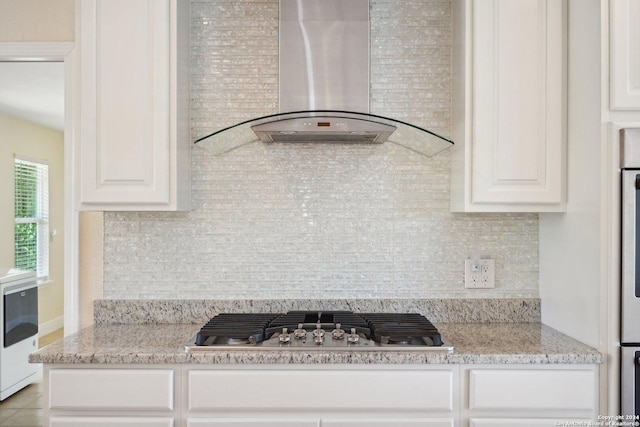 kitchen with tasteful backsplash, stainless steel gas cooktop, wall chimney range hood, and light stone countertops