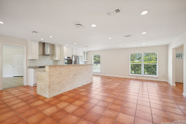 kitchen with backsplash, stainless steel appliances, wall chimney range hood, white cabinets, and light tile patterned flooring