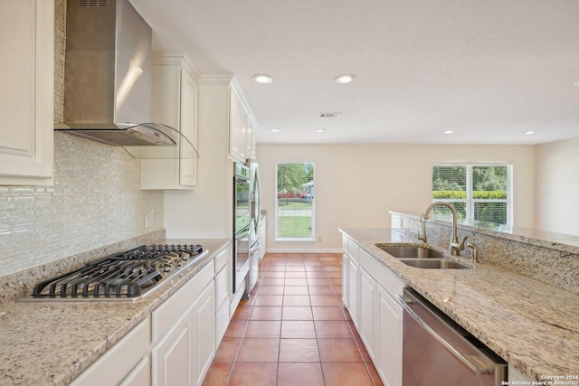 kitchen with white cabinets, wall chimney exhaust hood, appliances with stainless steel finishes, light stone countertops, and a sink