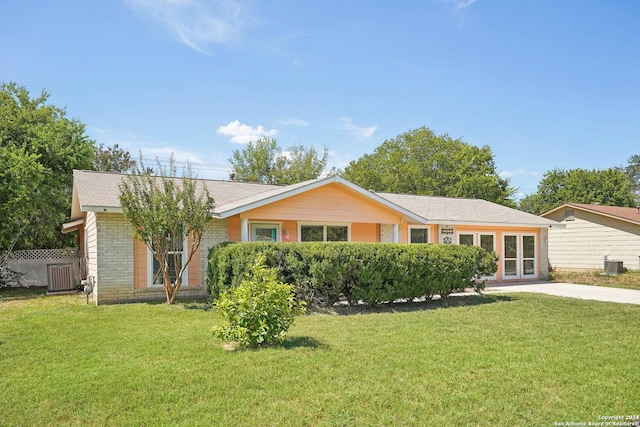 ranch-style home featuring cooling unit, brick siding, fence, and a front yard