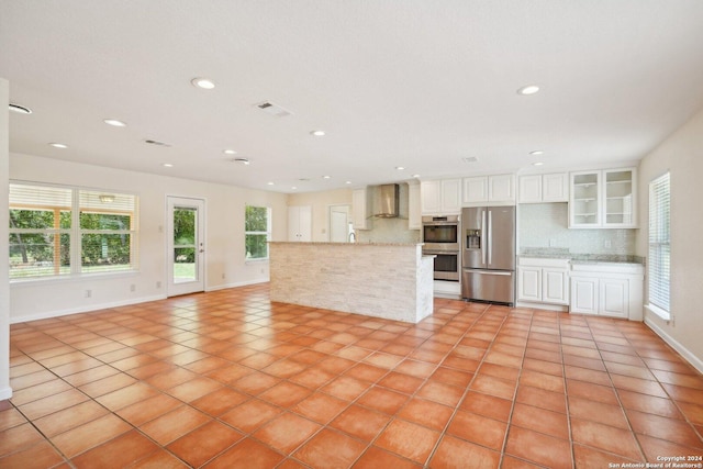 kitchen with appliances with stainless steel finishes, glass insert cabinets, white cabinetry, wall chimney range hood, and light stone countertops