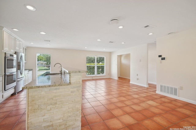 kitchen with a center island with sink, visible vents, white cabinets, a sink, and light stone countertops